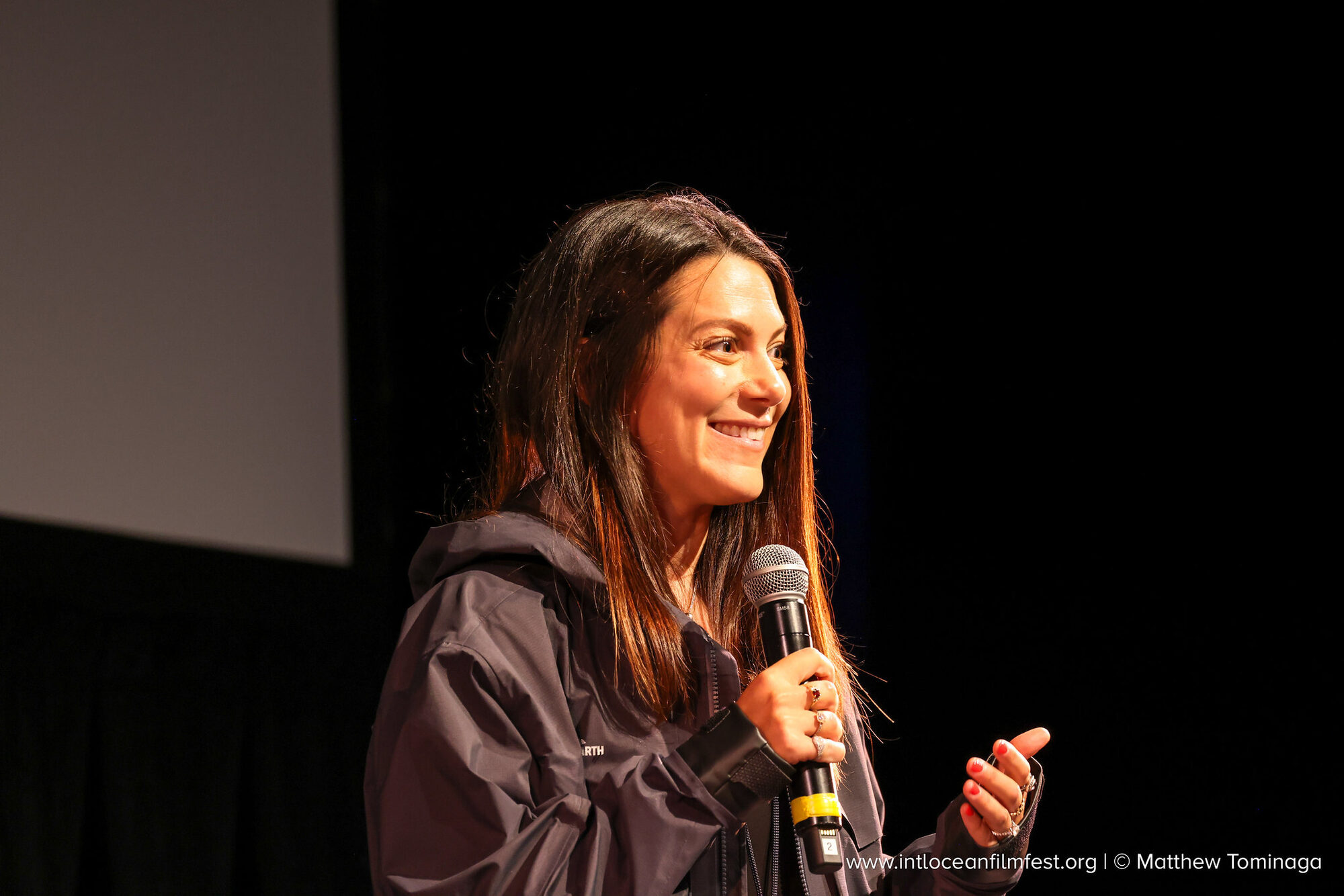 Andi Cross smiling while speaking on stage with a microphone